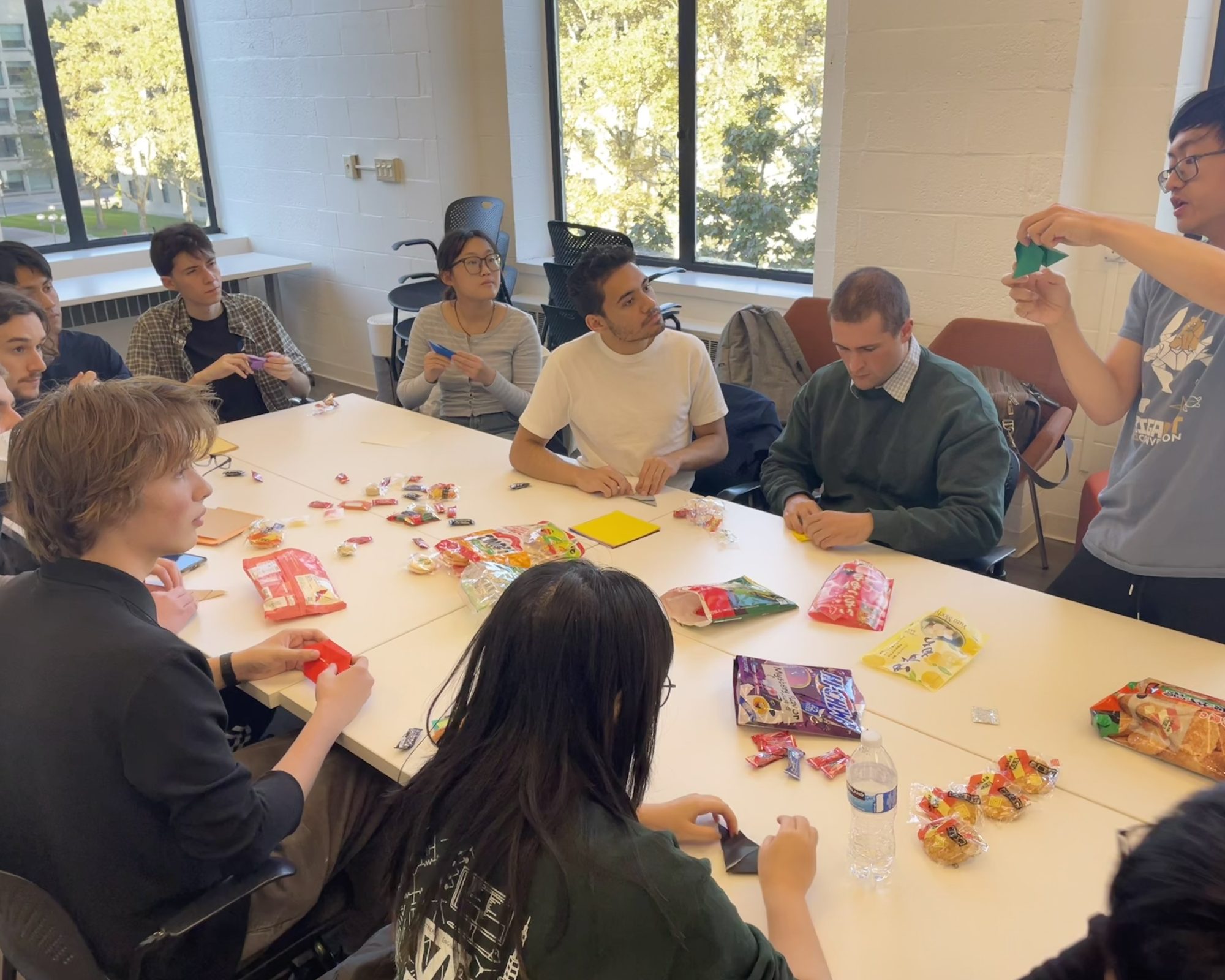 ten people around a table demonstrating origami projects