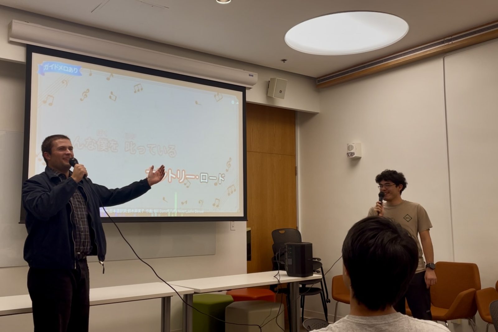 two people singing in front of a projection screen, holding microphones